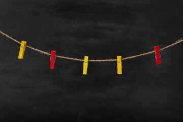 Red and yellow clothespins on rope on black background. Space for text, mock up