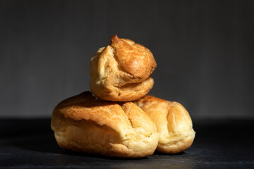 Delicate profiteroles or eclairs without cream. Close up. Black background.