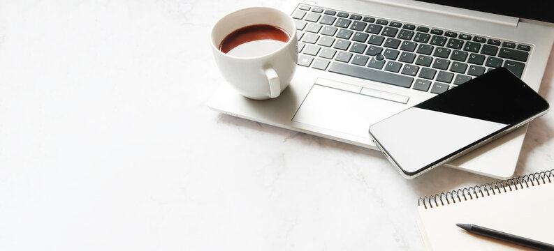 White office desk with a laptop, smartphone, notebook, pencil and a cup of coffee. With copy space for text.