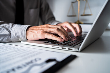 Law firm office, close-up view of businessman or lawyer using a laptop with contract paper, working...