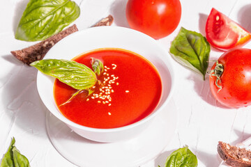 Bowls with homemade tomato soup. Ripe vegetables, fresh basil leaves, breadsticks, aromatic spices