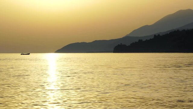 Golden hour sunset panoramic view of Mediterranean coastline, fishing boat returning on shore