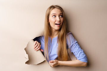 Beautiful young woman looking through a hole in beige paper