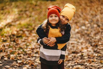 Two happy cheerful children friends in warm clothes play together have fun have fun and hug walking through the foliage in the fall park in nature golden autumn