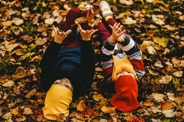 Two happy cheerful children friends in warm clothes play together have fun have fun and hug walking through the foliage in the fall park in nature golden autumn