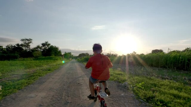 Rearview of Child riding a bicycle on the road rural in the evening. 10-year-old boy, Asian Thailand