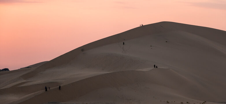 Panoramic view of people climbing the huge sand dunes in Badr, Medina, in Saudi Arabia at sunset