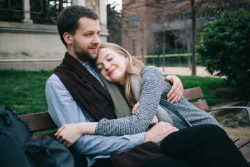 Cheerful couple hugging each other on bench - obrazy, fototapety, plakaty