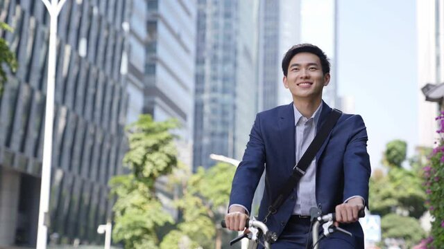 happy young asian businessman commuting by bike in modern city