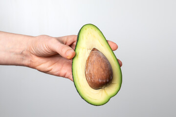 Cut in half avocado in a woman's hand on a light background