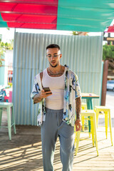 Chico joven atractivo tatuado con camisa de flores en local de playa en dia soleado de verano
