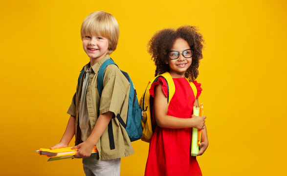 children with school backpacks are looking at the camera, holding books and pencils in their hands