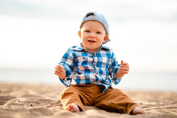 Cute baby boy sitting on the sand on the beach at sunset