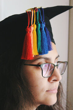 Portrait of young woman with graduation cap and tassels arranged as lgbtq rainbow pride flag colors