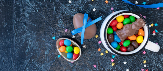 Obraz na płótnie Canvas banner with various chocolate candies in white mug on black texture background. egg-shaped sweets and chocolate rabbit. top view flat lay.