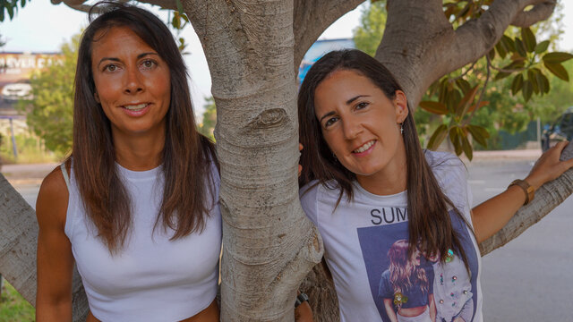 Dos chicas j&oacute;venes que son pareja celebran su aniversario de boda con la bandera LGBTI de fondo en un parque verde y frondoso