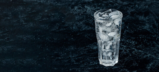 banner with glass with ice water and ice cubes on a black textured background. A refreshing and chilling drink in hot weather.