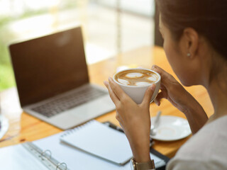 Close up female drink hot coffee at co-working space, businesswoman drink coffee while watch business strategy video