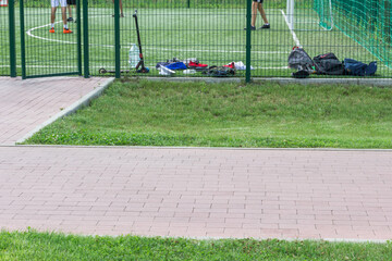 Sports ground for playing football. Players 'backpacks near the fence, footballers' feet on  field.