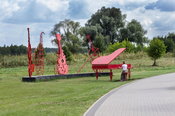 Orchestra installation in park, red piano, cello and violin. Woman imitates playing the piano