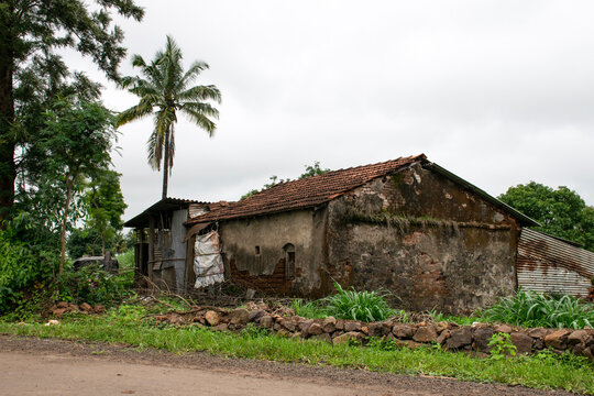 Stock photo of old, damaged red brick house with pyramid shape roof top in very green landscape of village area, at Kolhapur Maharashtra India.