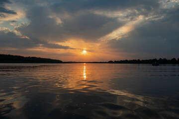 Obraz premium Red sunset on the river. Evening. The rays of the sun in the clouds