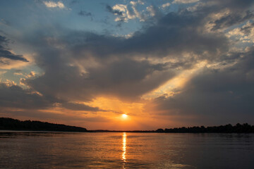 Red sunset on the river. Evening. The rays of the sun in the clouds