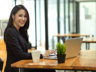 Elegant businesswoman in black suit typing on laptop keyboard at cafe