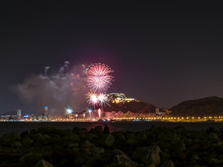 Night cityscape with fireworks from a rocky beach with somebody observing