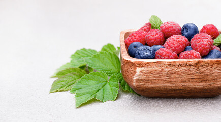 raspberries and blueberries in a wooden plate on a concrete background