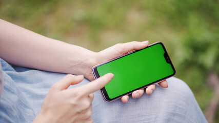 Businesswoman holds in hands close up and uses cellular telephone with touch green screen for reading press by media or social networks closeup. Hands with a smartphone close up, hromakey