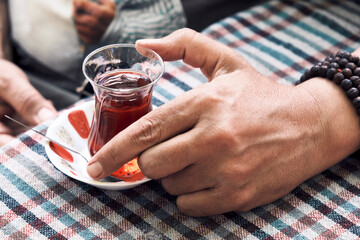Hand of a male holding a traditional pear shaped glass of Turkish tea