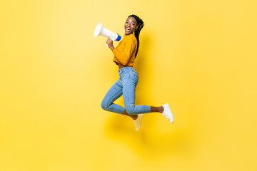 Joyful young African American woman holding megaphone jumping and making announcement in isolated...
