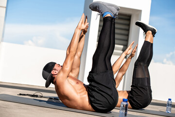 Group of athletic men doing toe touch crunch workout exercise outdoors on building rooftop floor