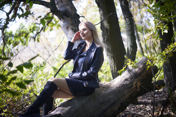 Sexy young woman in a little black dress and biker jacket relaxing in nature