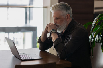 an incredibly beautiful and stylish gray-haired man of fifty years old working with a laptop, a...