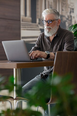 an incredibly beautiful and stylish gray-haired man of fifty years old working with a laptop, a...
