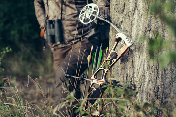 Close up shot of a hunter dressed in camouflage clothing holding a modern bow.
