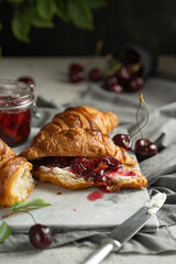 Freshly baked croissants with homemade berry jam, cheese cream, fresh cherries on white chopping board, dark background. Selective focus, copy space. Beautiful breakfast or dessert.  Sweet pasty