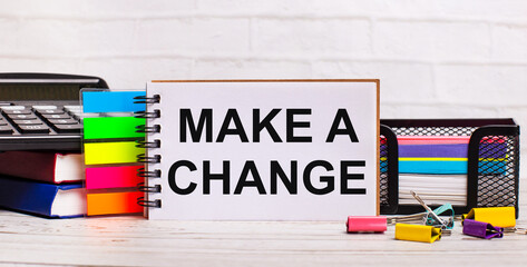 On a light wooden background, a calculator, multi-colored sticks and a notebook with the text MAKE...