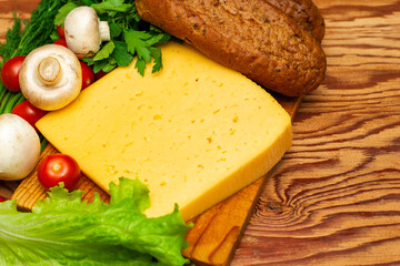 a piece of cheese greens lettuce cherry tomatoes mushrooms and rye buns on a wooden cutting board on the copyspace table