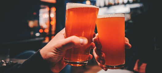 Closeup view of a two glass of beer in hand. Beer glasses clinking in bar or pub