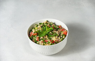 Eastern Tabouleh salad cooked in a white plate with boiled bulgur, mint, lemon, tomatoes, cilantro, green onions, parsley, seasoned with olive oil. On white background. Minimalism.
