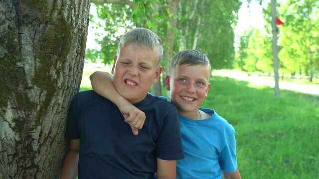 Two boys, 10 and 12 years old, hug and play with each other in front of the camera. Best friends. Happy childhood. Outdoor weekend
