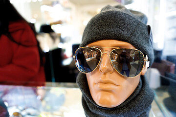 White mannequin dummy head with set dark grey hat and scarf and black glasses in store or mall showcase