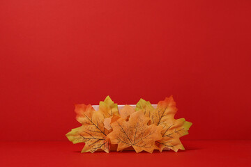 Modern Autumn podium with decor falling leaves on red background