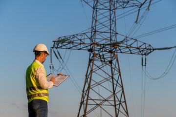 Engineer checking power lines plan in field at sunset
