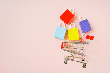 side of shopping cart and small multi colored shopping bags on pink background