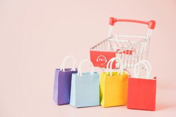 multi color shopping bags and blurred shopping cart with 24 hours 7 days service sign on pink...