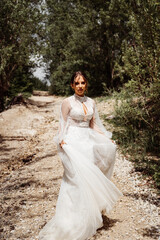 Fototapeta na wymiar woman in wedding dress walks along mountain path between trees.